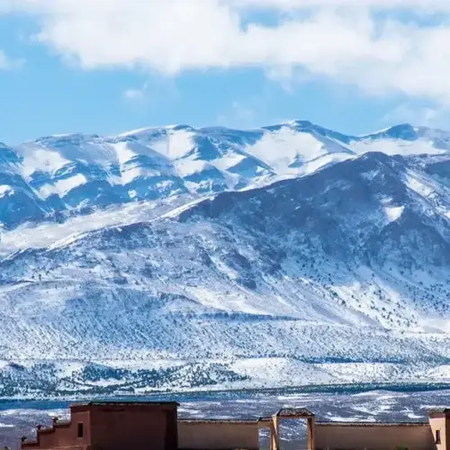 Snow-capped peaks of the High Atlas Mountains rising above a traditional earthen kasbah building on the open plain below, Morocco