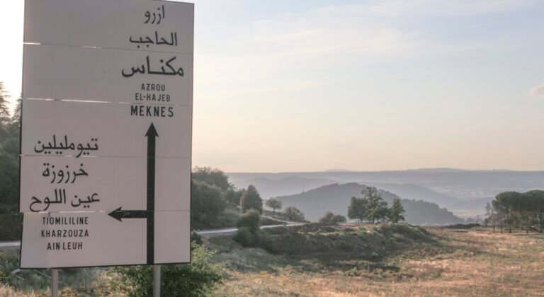 A bilingual Arabic and French directional road sign at a rural intersection in Morocco, showing distances to nearby towns
