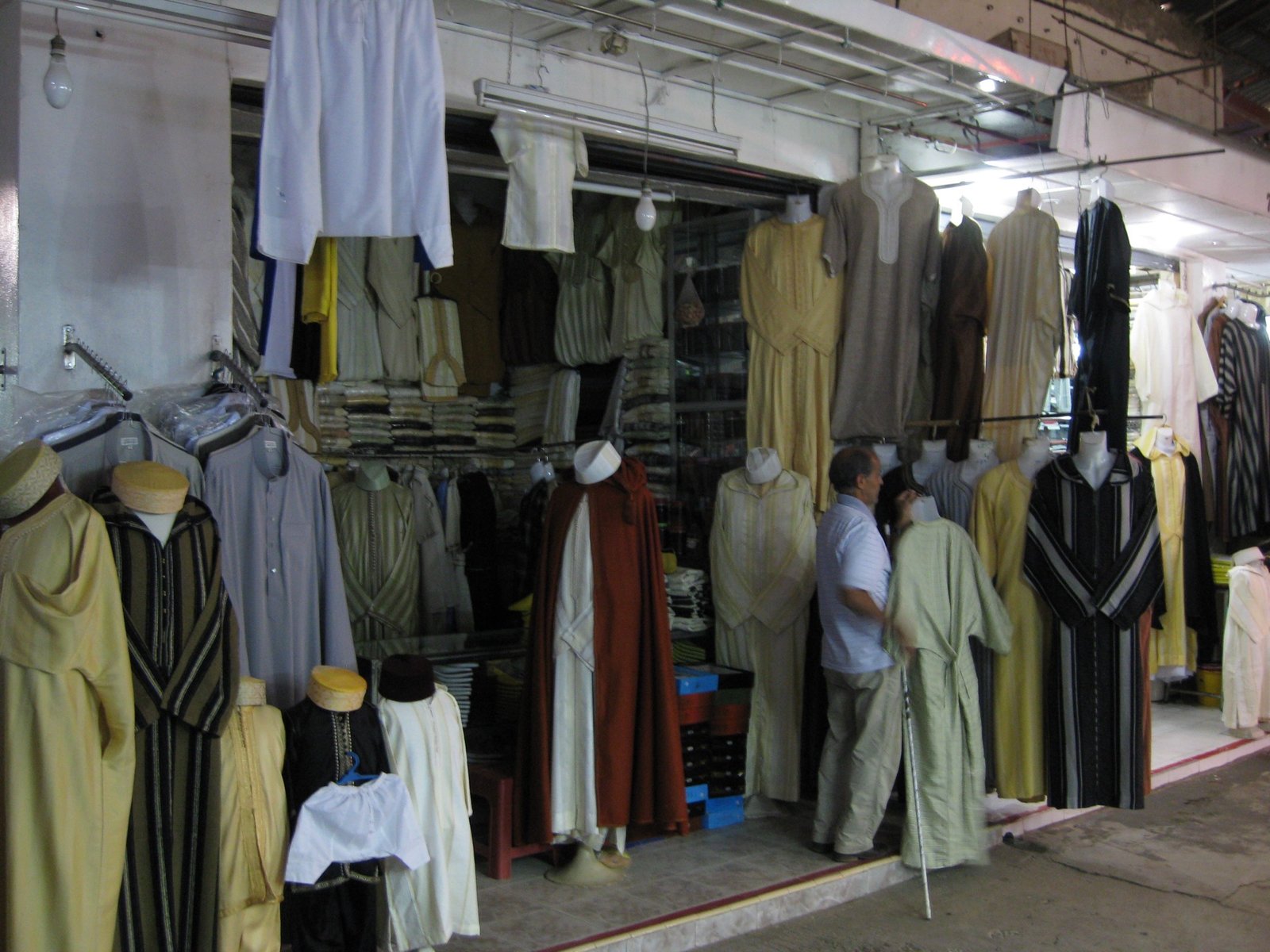 A market stall in Agadir displaying traditional Moroccan djellabas, kaftans, and robes for sale, the kind of loose, modest clothing that inspired local dress norms
